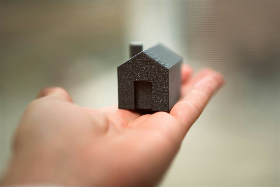 Mão segurando a miniatura de uma casa